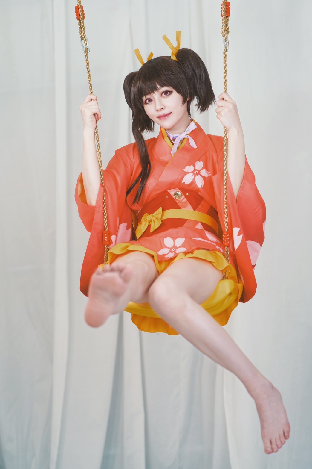 白い布背景で赤い衣装のコスプレイヤーがブランコに乗る撮影作品